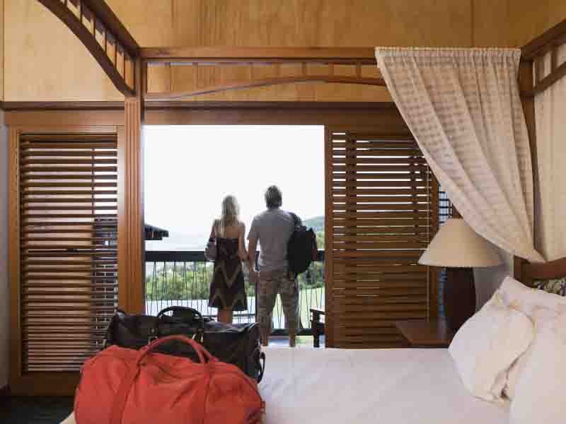 A man and woman looking outside from window of a hotel room